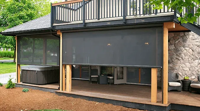 Outdoor home patio with a gray retractable shade, stone walls, and a hot tub on the left