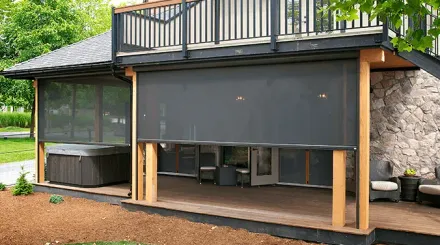 Outdoor home patio with a gray retractable shade, stone walls, and a hot tub on the left