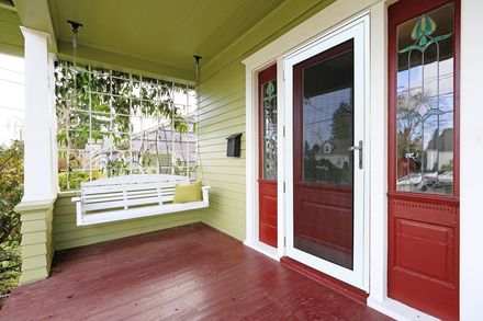 Front porch with red floor, white swing bench, and red-trimmed glass door on a green house.