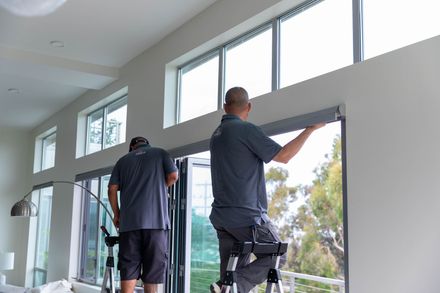 Two workers installing a large window frame in a bright interior space