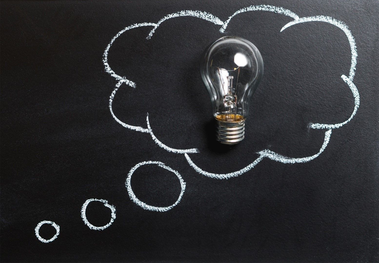 Lightbulb inside a white chalk-drawn thought bubble on a black chalkboard.