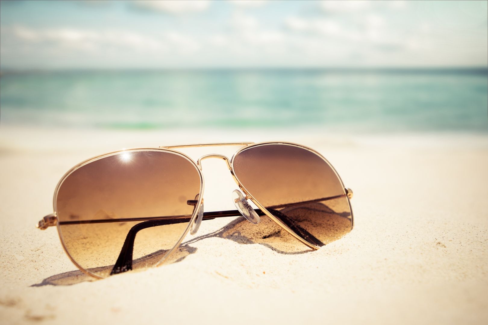 Sunglasses on sandy beach with ocean in background.