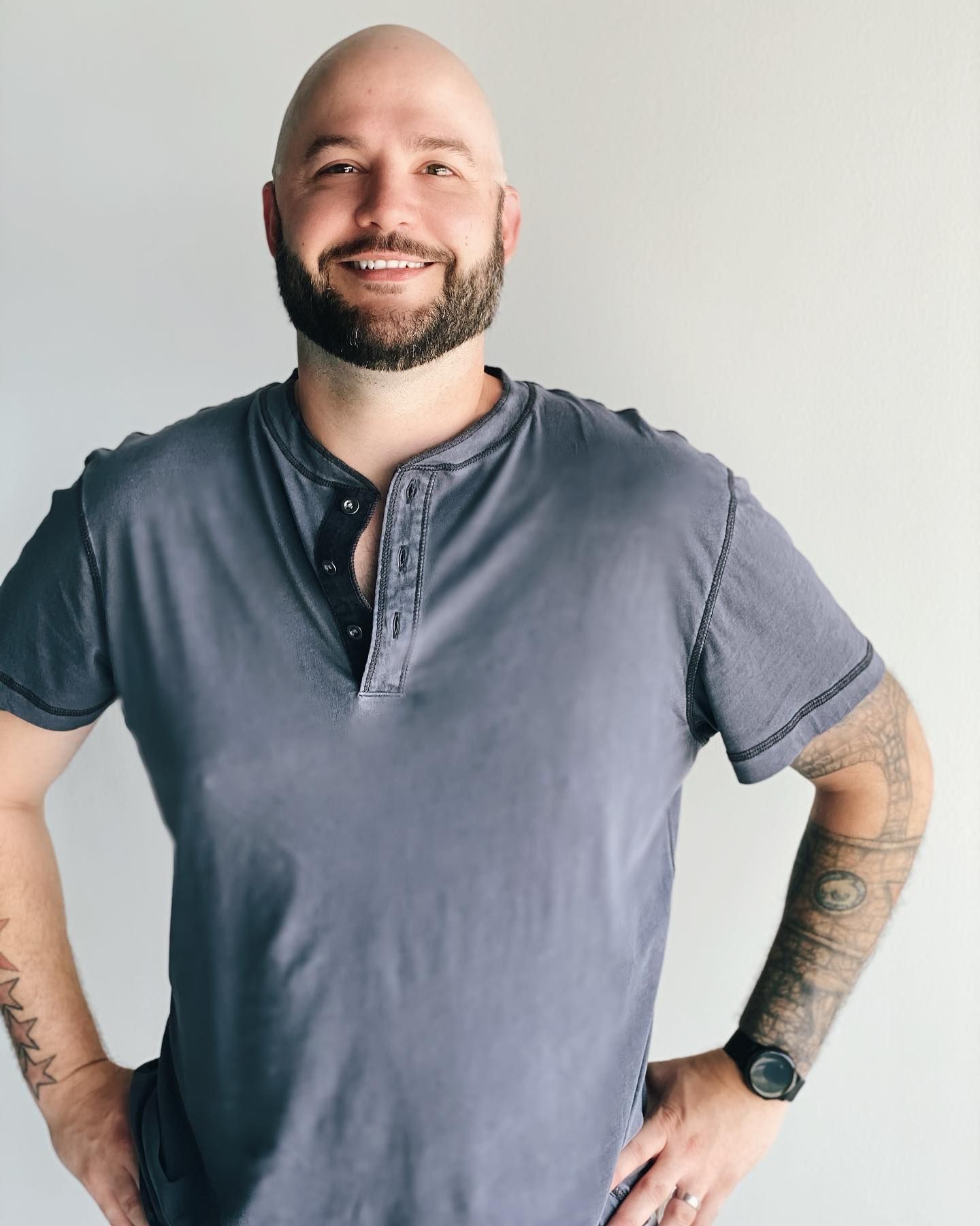 A bald man with a beard wearing a grey shirt and a watch