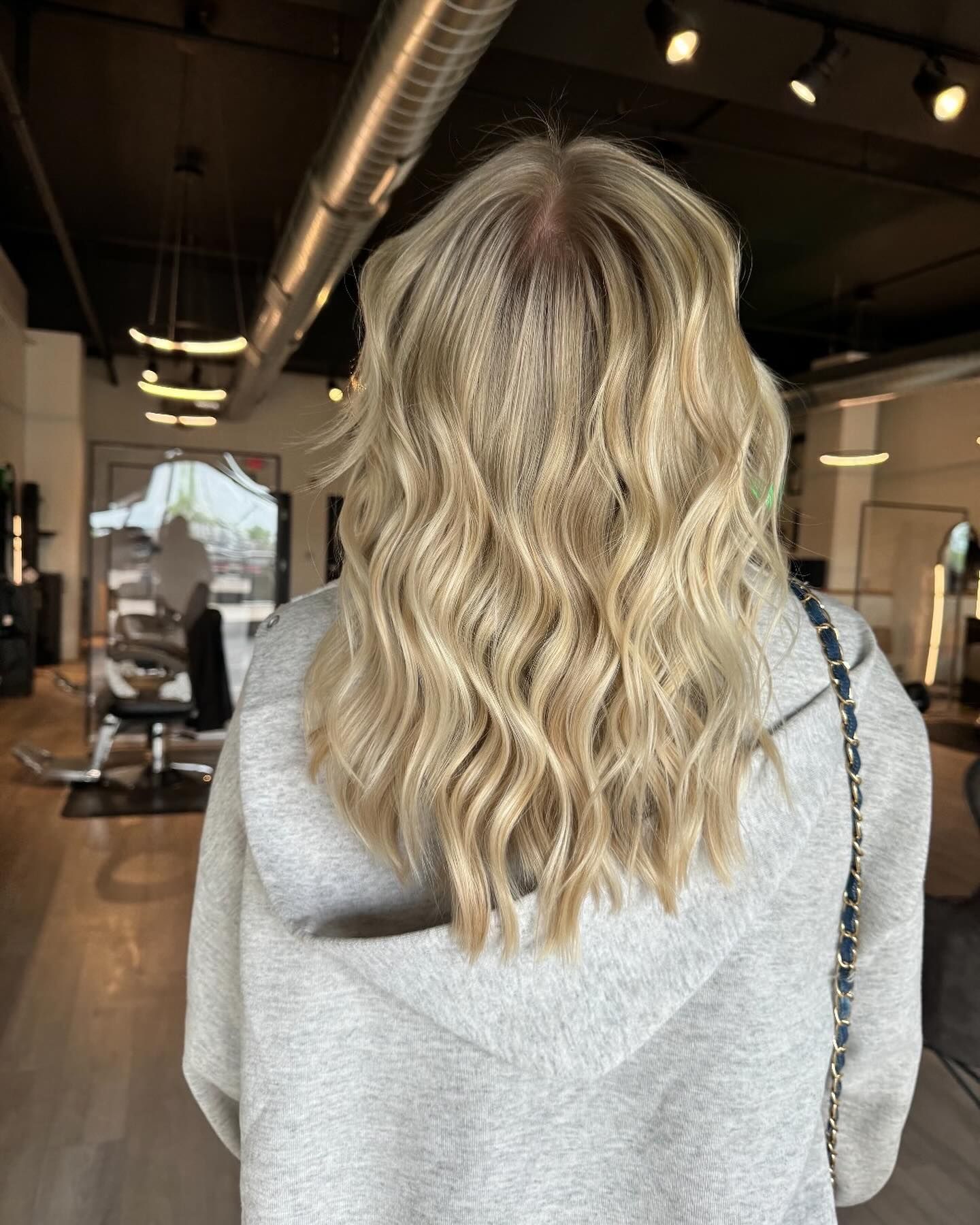 A woman with blonde hair is standing in a salon wearing a grey hoodie.