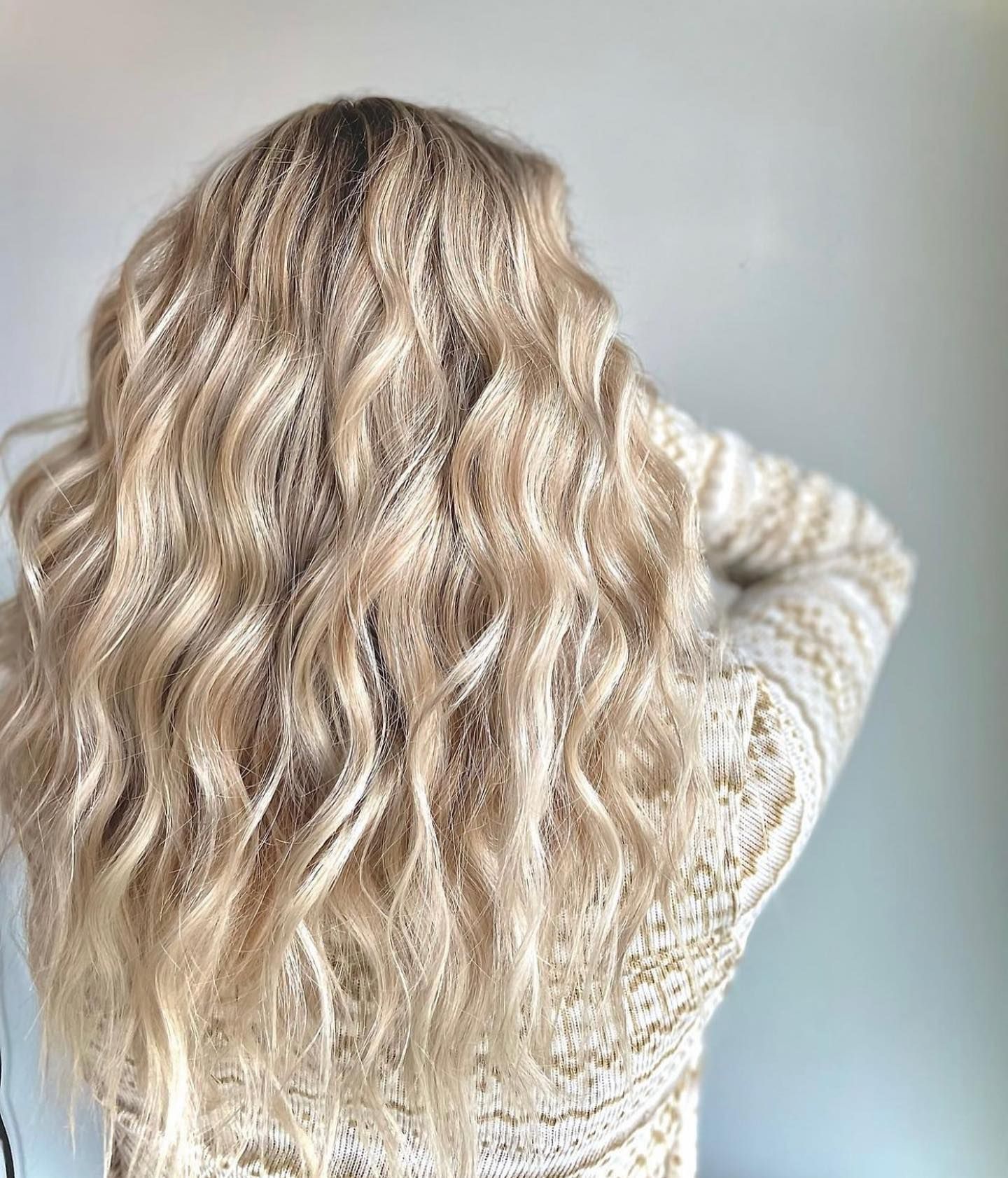 A woman with long blonde wavy hair is wearing a white sweater.
