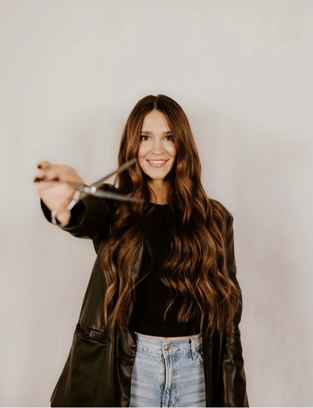 A woman with long hair is wearing a tan jacket and smiling.