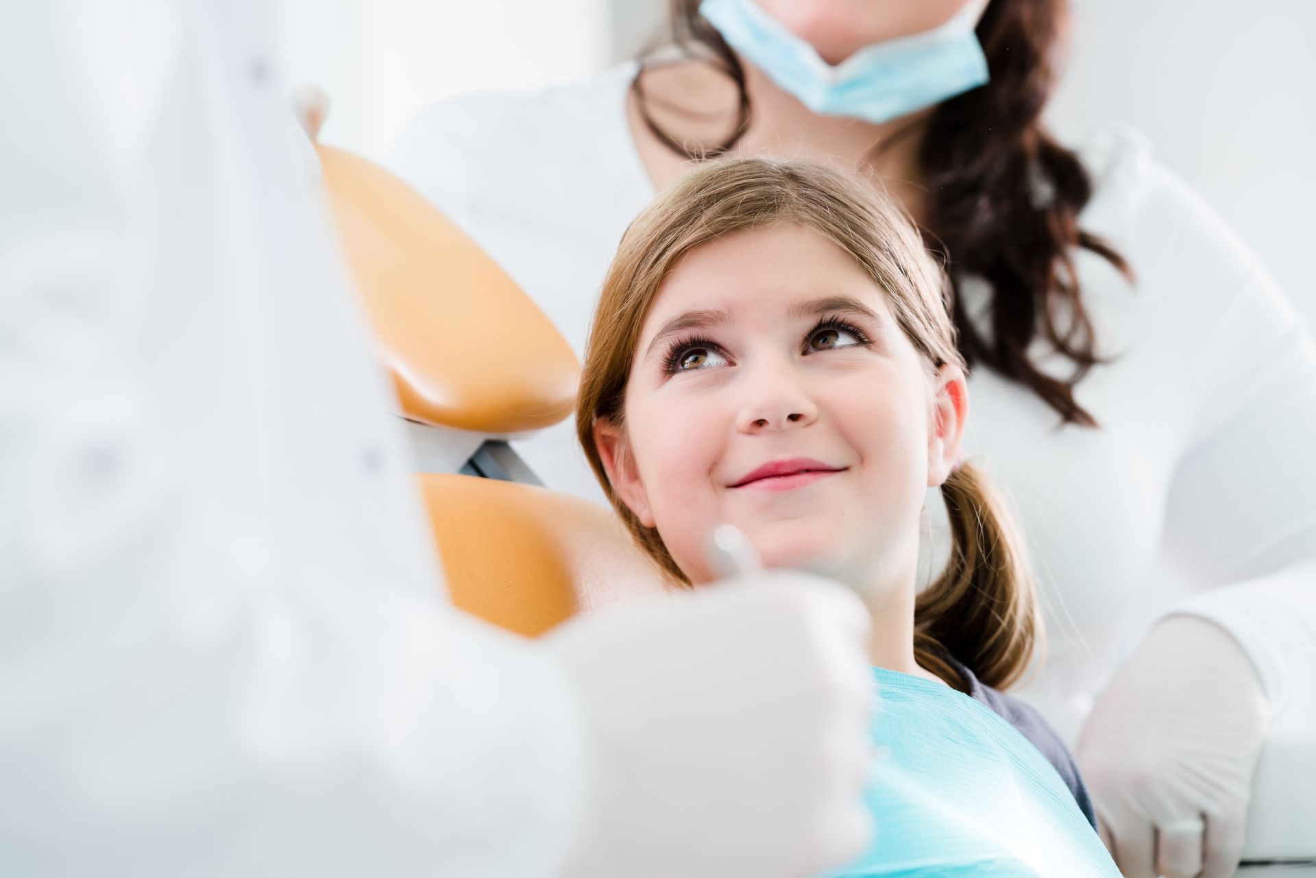 Smiling child in a dentist chair looking up at a masked dental professional Smiling child in a dentist chair looking up at a masked dental professional