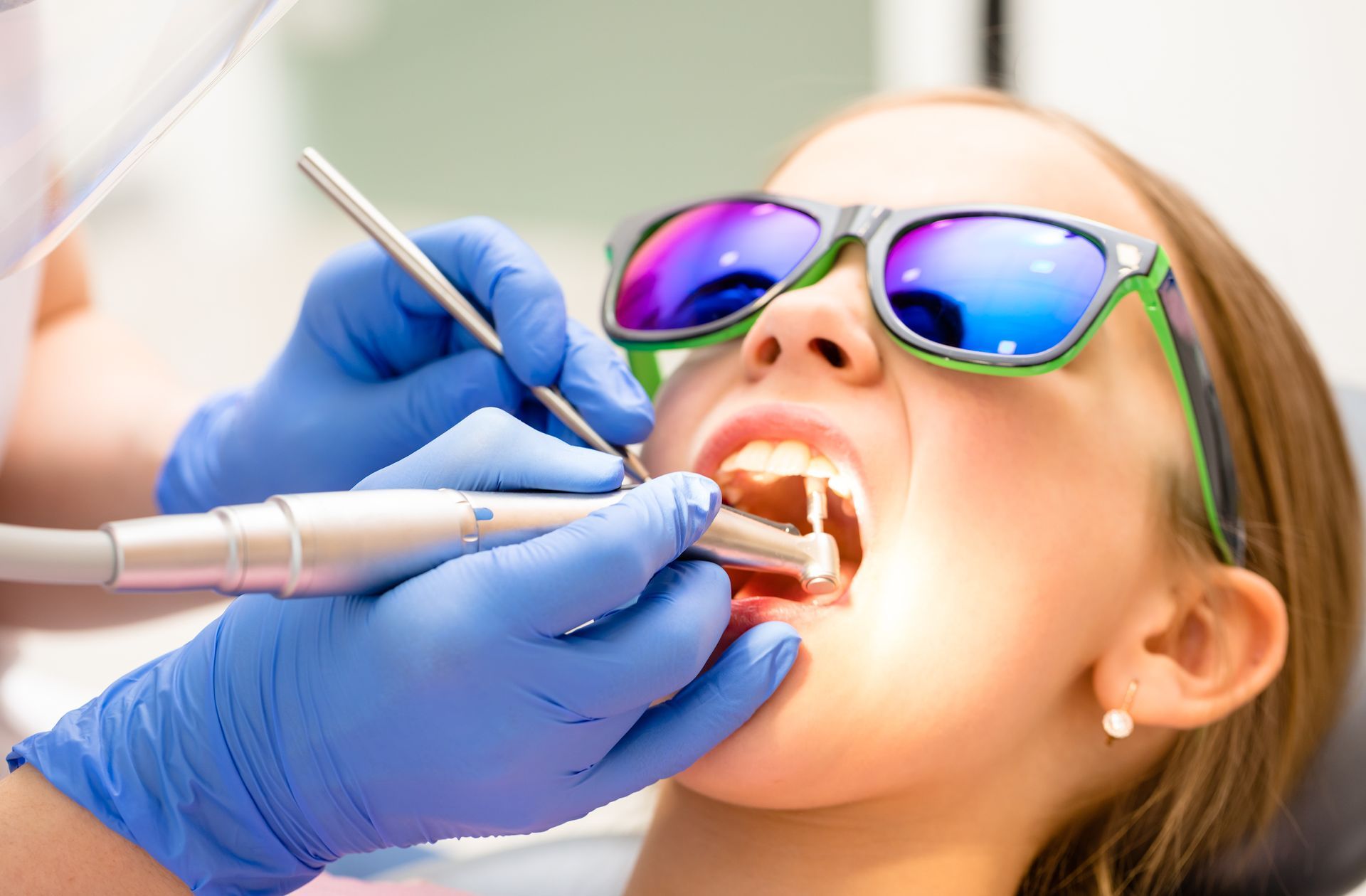 Dentist examining a patient’s open mouth with dental tools and blue gloves Dentist examining a patient’s open mouth with dental tools and blue gloves
