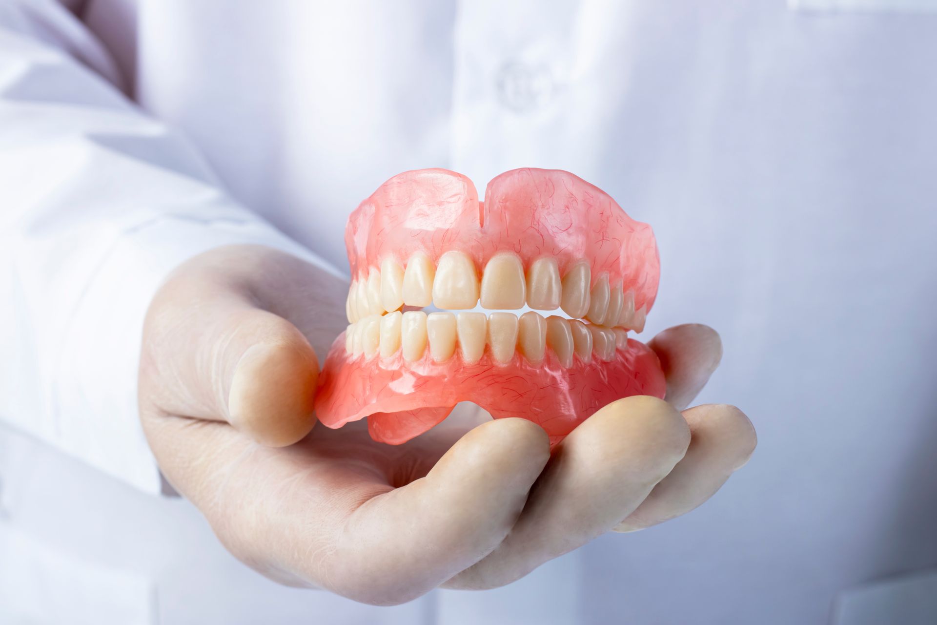 Dentist holding upper and lower dentures in gloved hands against a white background Dentist holding upper and lower dentures in gloved hands against a white background