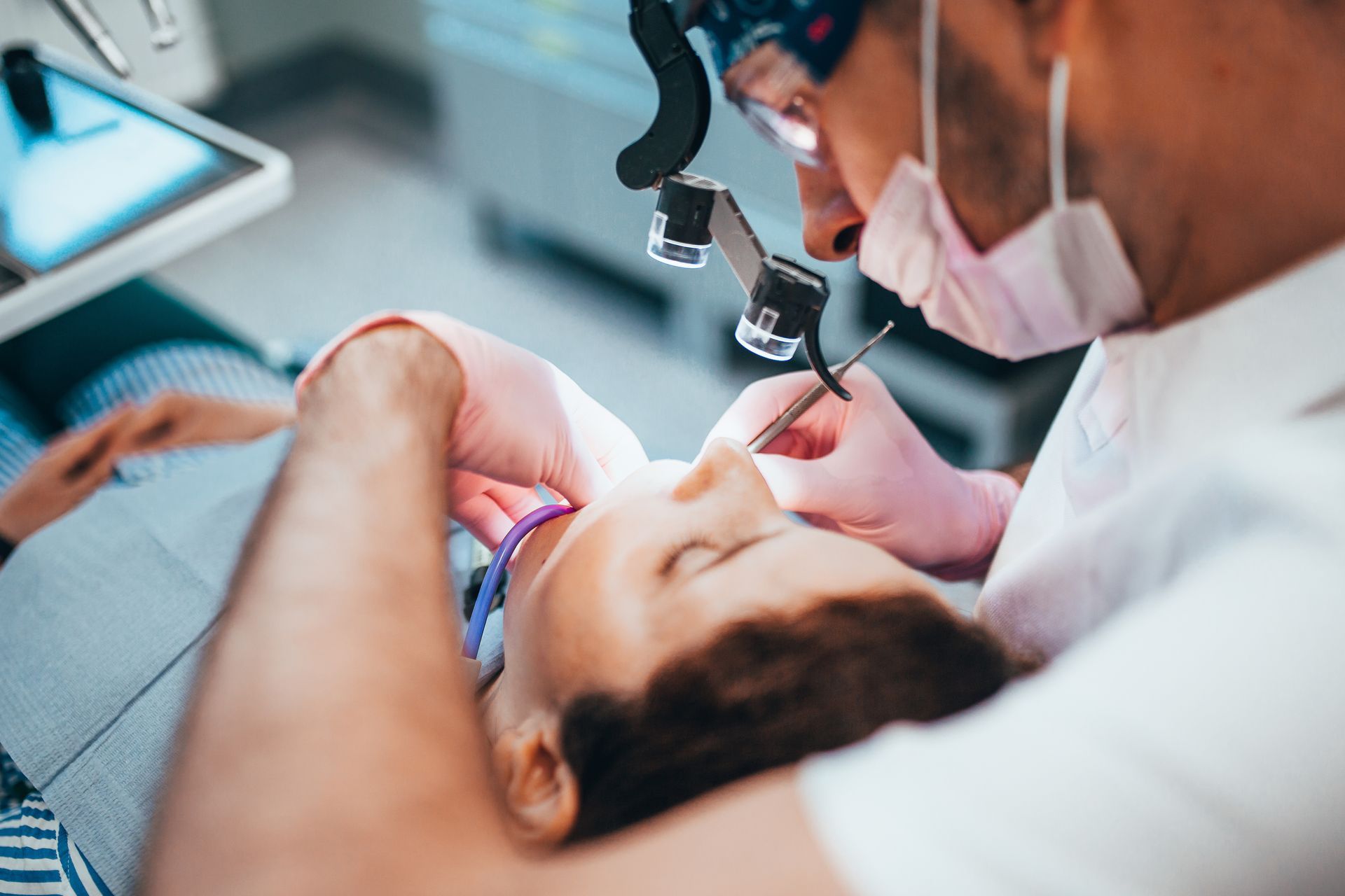 Dentist examining a patient during a procedure with dental tools and magnification loupes