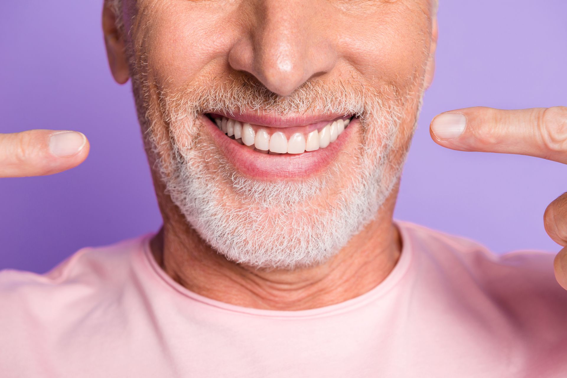 Smiling man in a pink shirt pointing at his teeth against a purple background Smiling man in a pink shirt pointing at his teeth against a purple background
