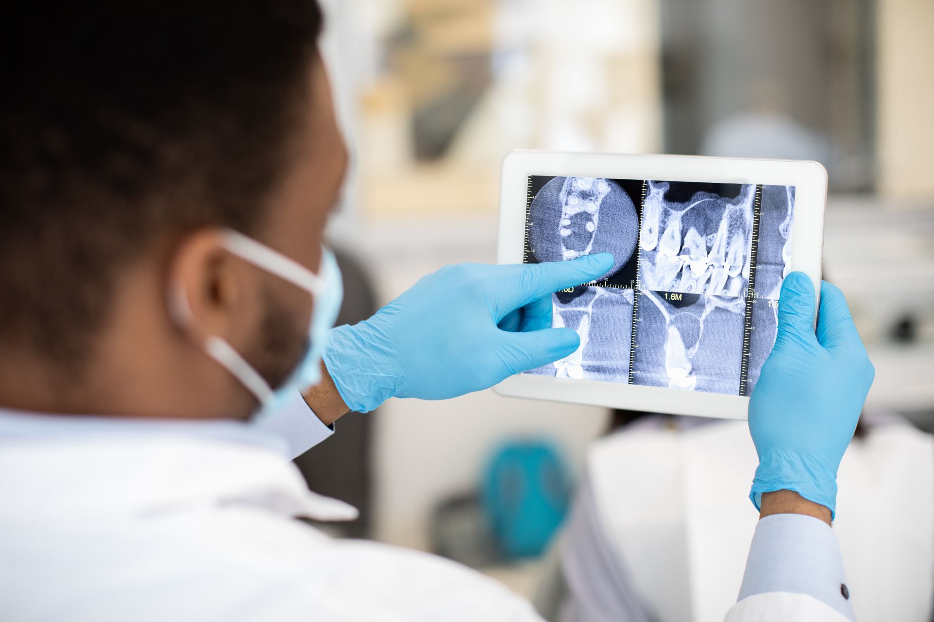 Dentist in blue gloves examining a dental X-ray on a tablet Dentist in blue gloves examining a dental X-ray on a tablet