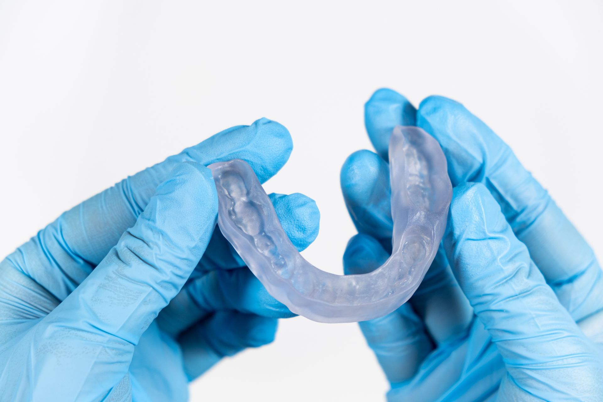 Blue-gloved hands holding a clear dental retainer against a white background Blue-gloved hands holding a clear dental retainer against a white background