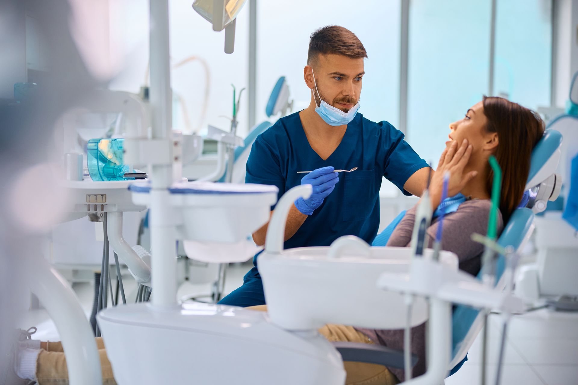 Dentist examining a patient in a bright dental clinic, wearing blue scrubs and gloves. Dentist examining a patient in a bright dental clinic, wearing blue scrubs and gloves.