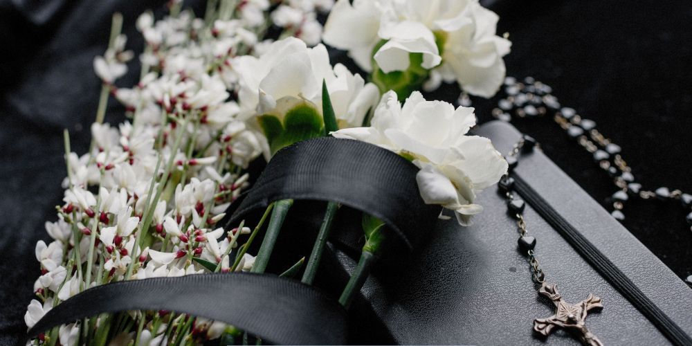 White sympathy flowers with black ribbon and a rosary cross symbolizing remembrance at a funeral home and cremation service in Hanover, PA.