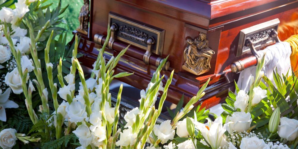 Wooden funeral casket surrounded by white floral arrangements at a funeral home and cremation service in McSherrystown, PA