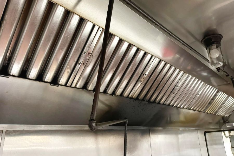 Stainless steel commercial kitchen exhaust hood with a full row of baffle filters seated back in place after cleaning