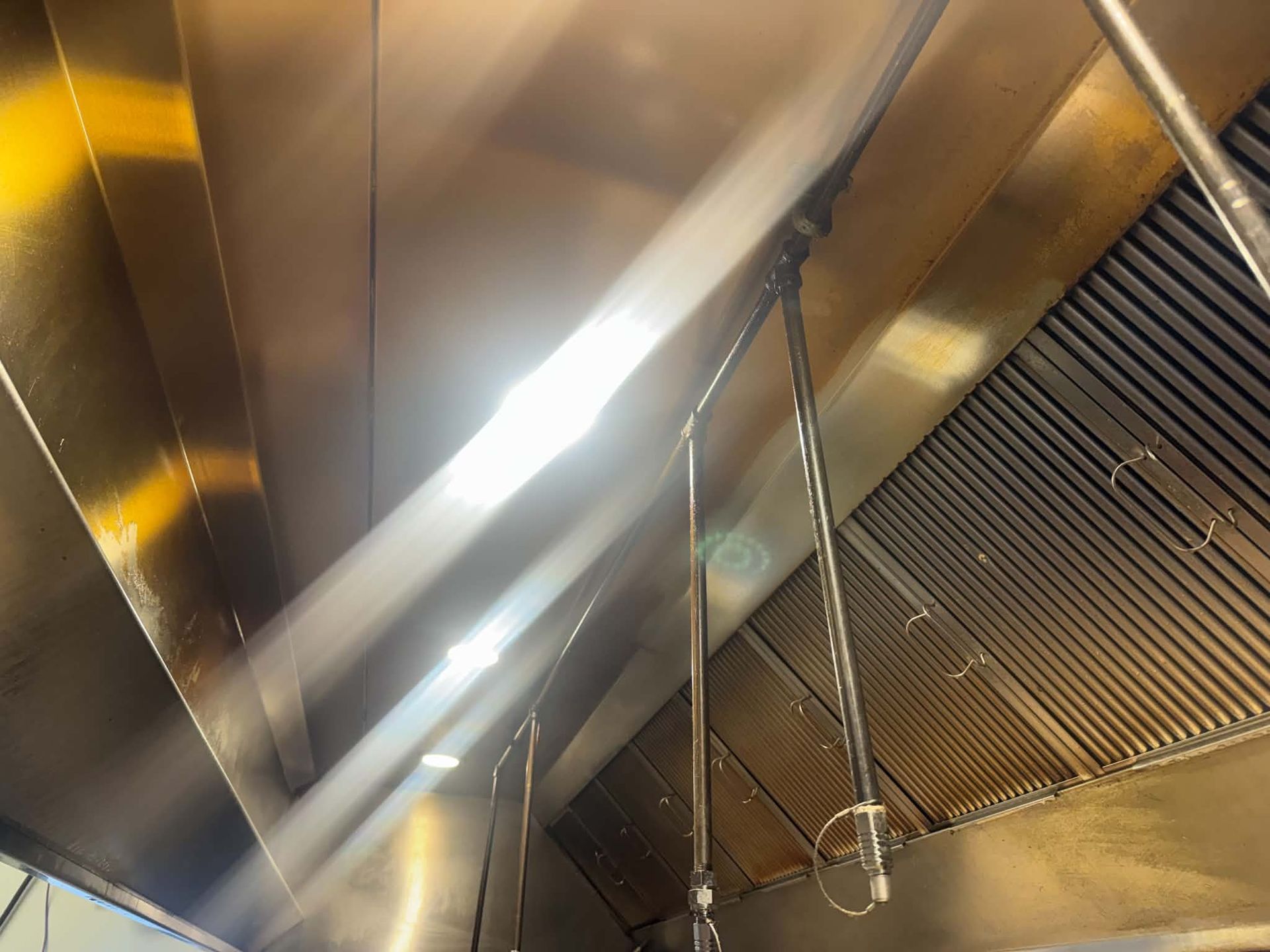 Row of stainless steel baffle filters coated in brown grease inside a commercial kitchen exhaust hood before cleaning