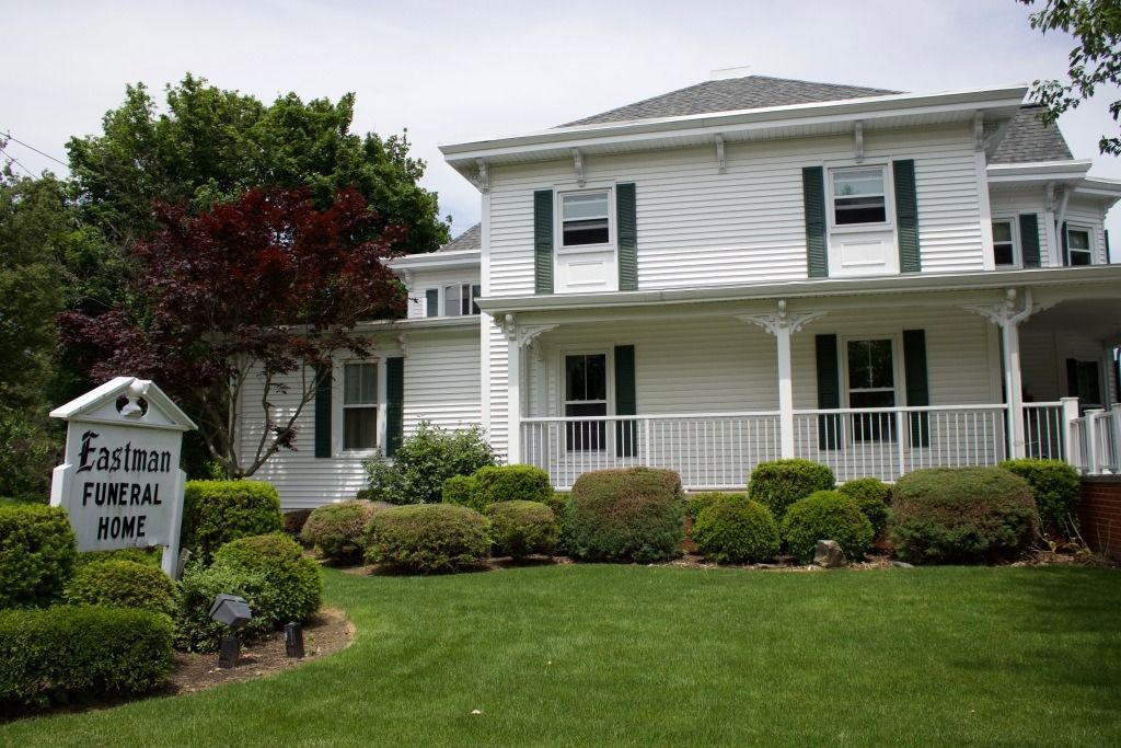 White two-story building with a porch, green shutters, and a sign that reads