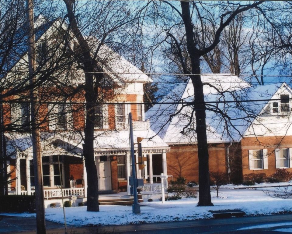 Snowy Victorian house with white porch and bare trees.