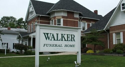 White sign for Walker Funeral Home in front of a brick building and green lawn.