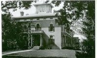 Elegant, three-story house with a tower, porch, and ornate details, framed by trees.