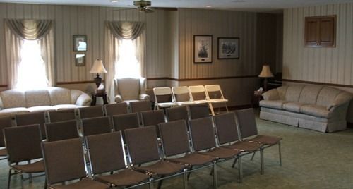 Interior of a room with rows of chairs facing sofas and windows; likely a waiting or meeting area.