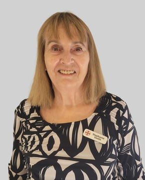 A person with light brown hair smiles while wearing a black and white patterned top and a small name tag on their chest.