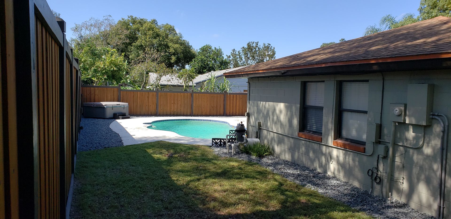 Backyard with a turquoise pool, lawn, wooden fence, and a house in bright sunlight