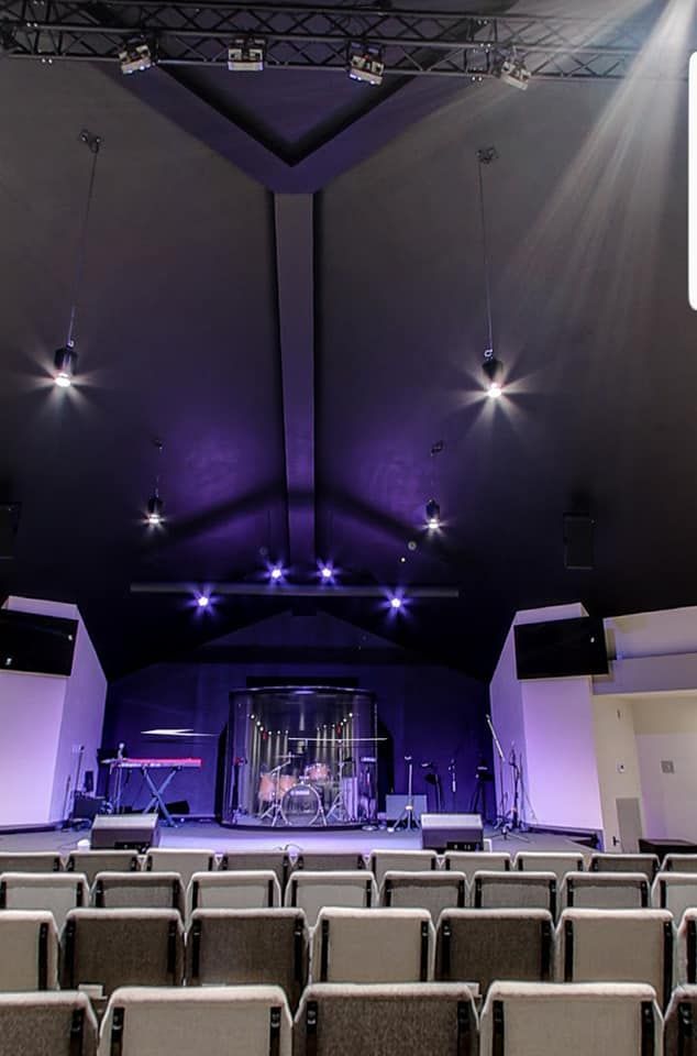 Empty auditorium with rows of seats facing a lit stage under purple lights