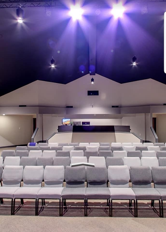 Empty modern auditorium with rows of white seats and purple stage lighting overhead