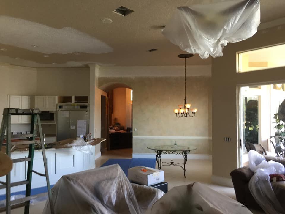 Unfinished living room with covered furniture, ladder, and kitchen area under renovation