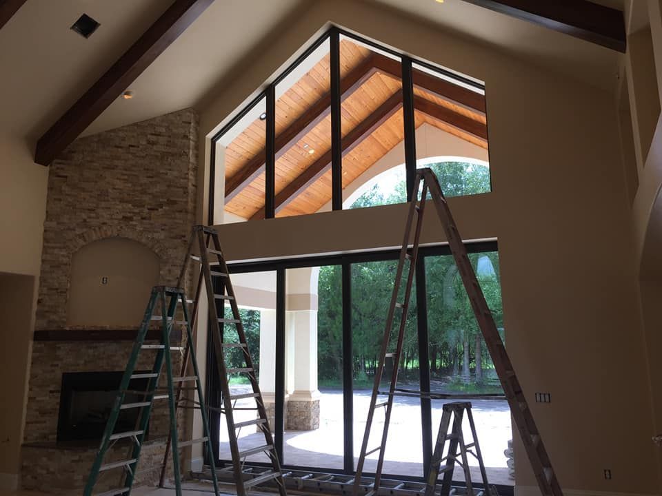 Living room with vaulted ceiling, ladders, and large windows during interior painting or renovation