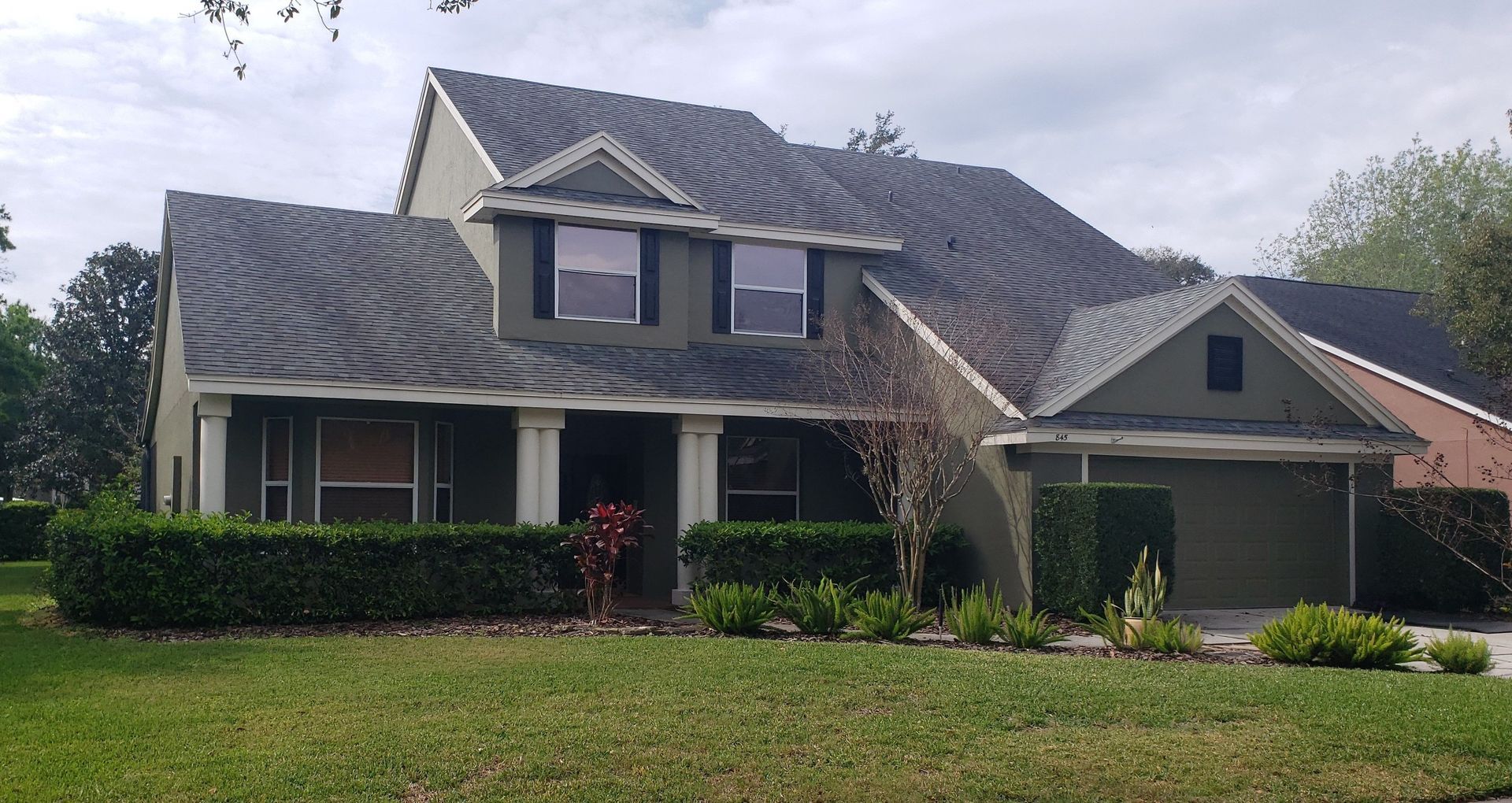 Two-story suburban house with gray siding, dark roof, front porch, and attached garage behind a green lawn