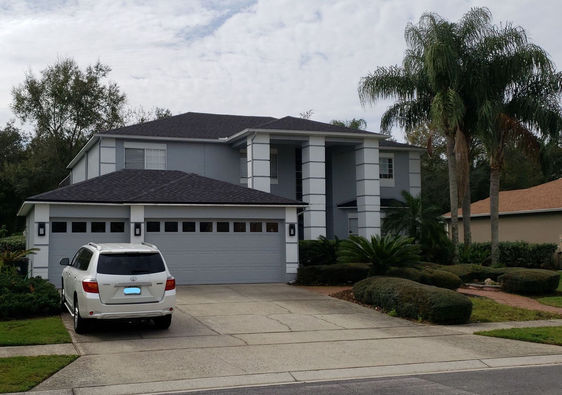 Suburban two-story house with a white SUV parked in the driveway and palm trees in front