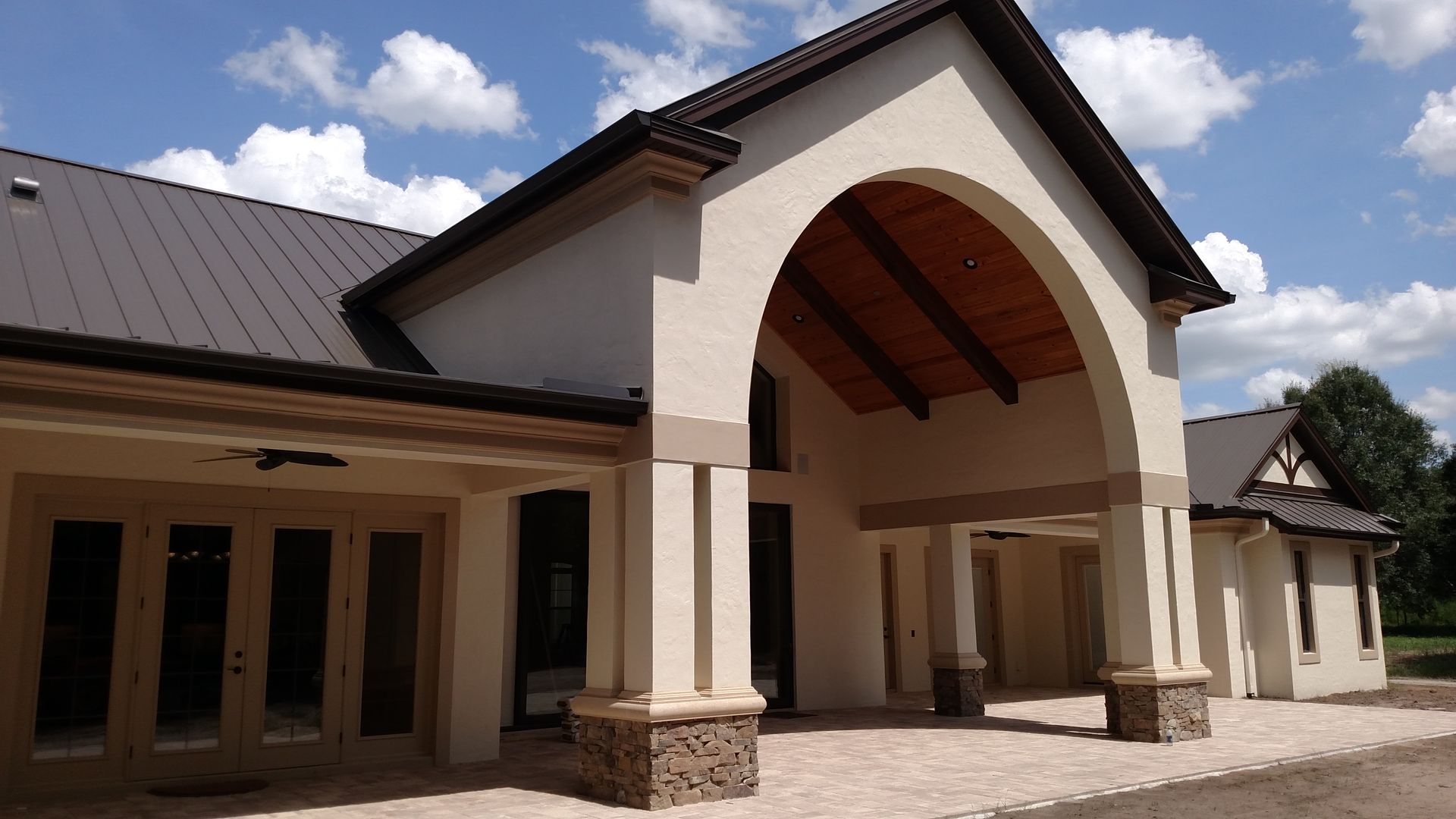 Modern building entrance with large arched portico, white columns, and dark metal roof under a partly cloudy sky