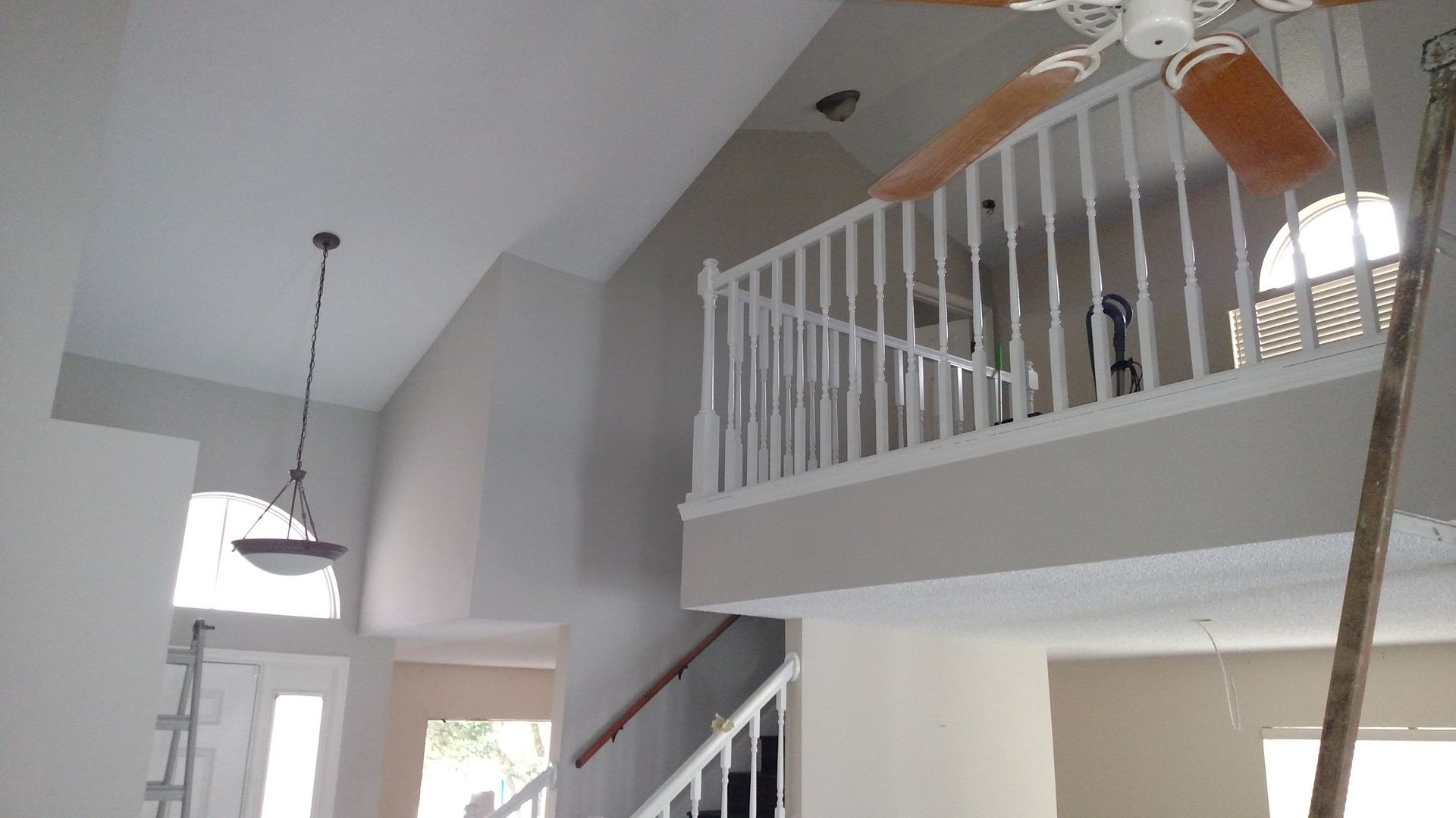 Bright foyer with vaulted ceiling, white railings, and ceiling fans above a staircase mezzanine