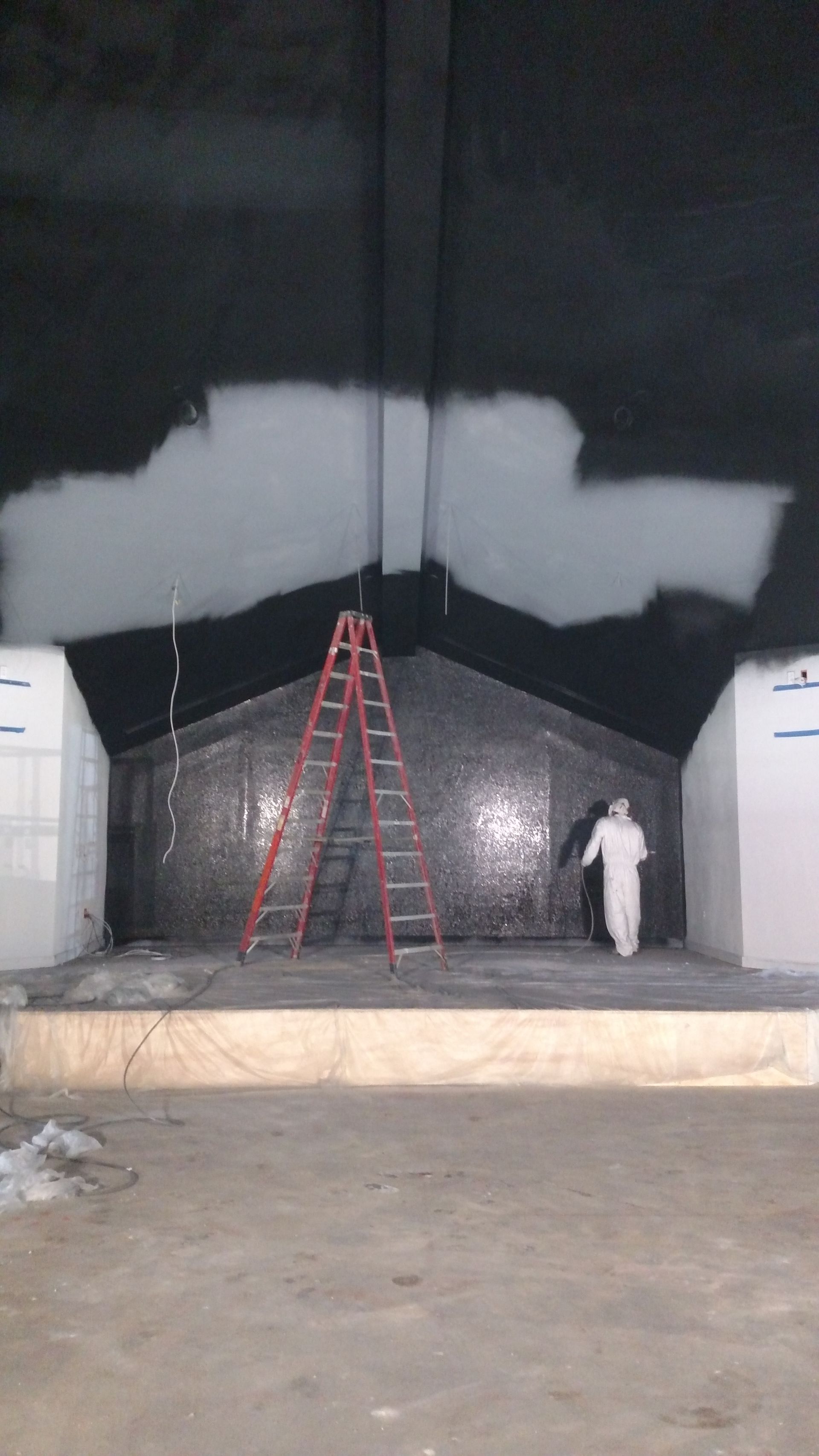 A red ladder stands against a dark wall, with a worker in white beside it and a white patch near the top.