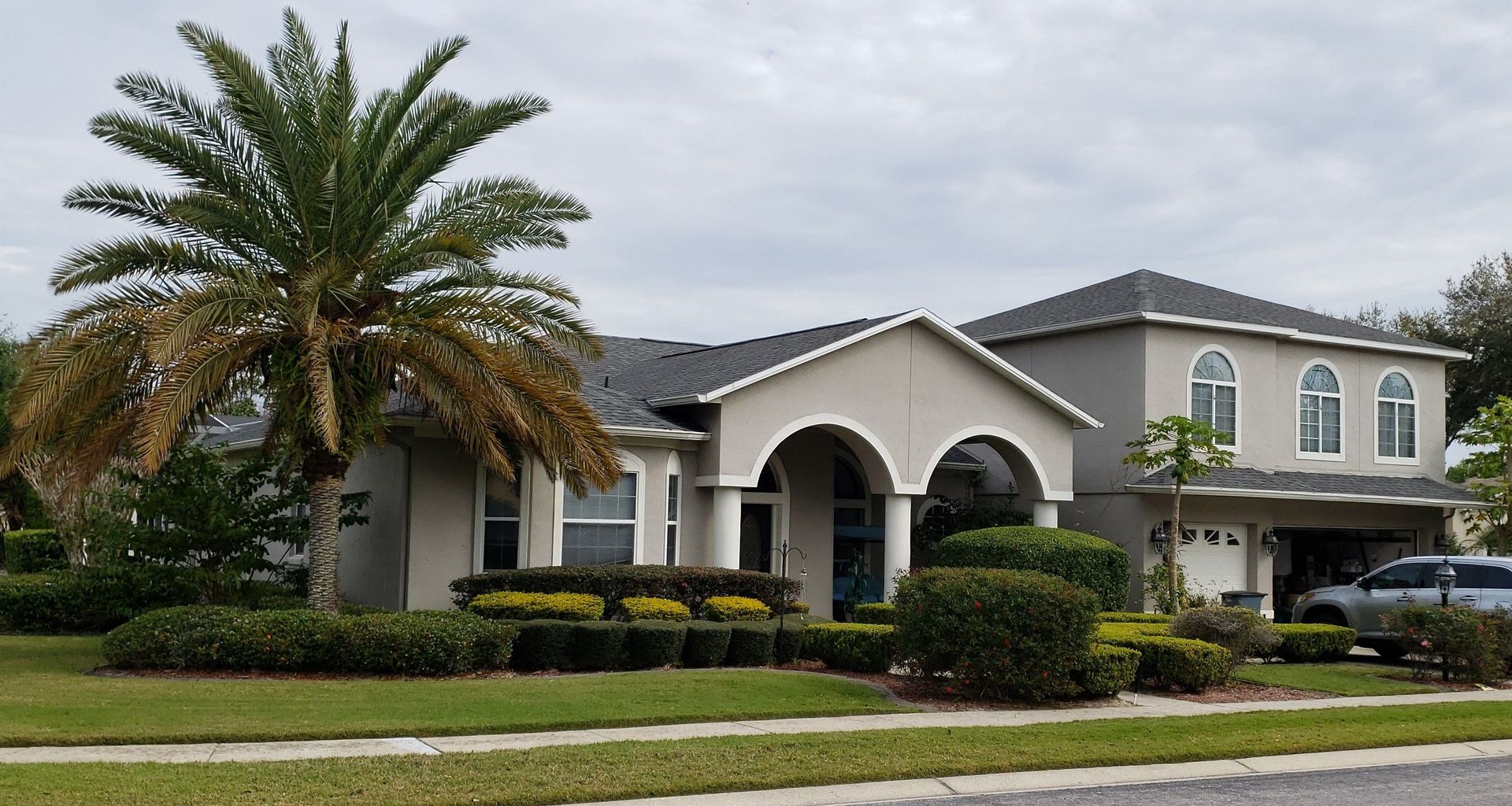 Suburban house with arched entry, palm tree, and manicured lawn on a quiet street