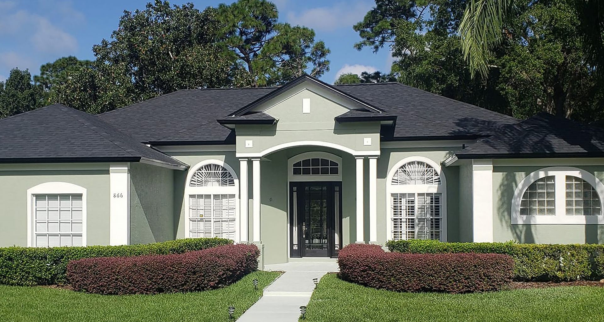 Single-story suburban house with white exterior, dark roof, and manicured hedges in front