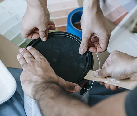 Hands adjusting a black circular lid on a container in a bright workspace.