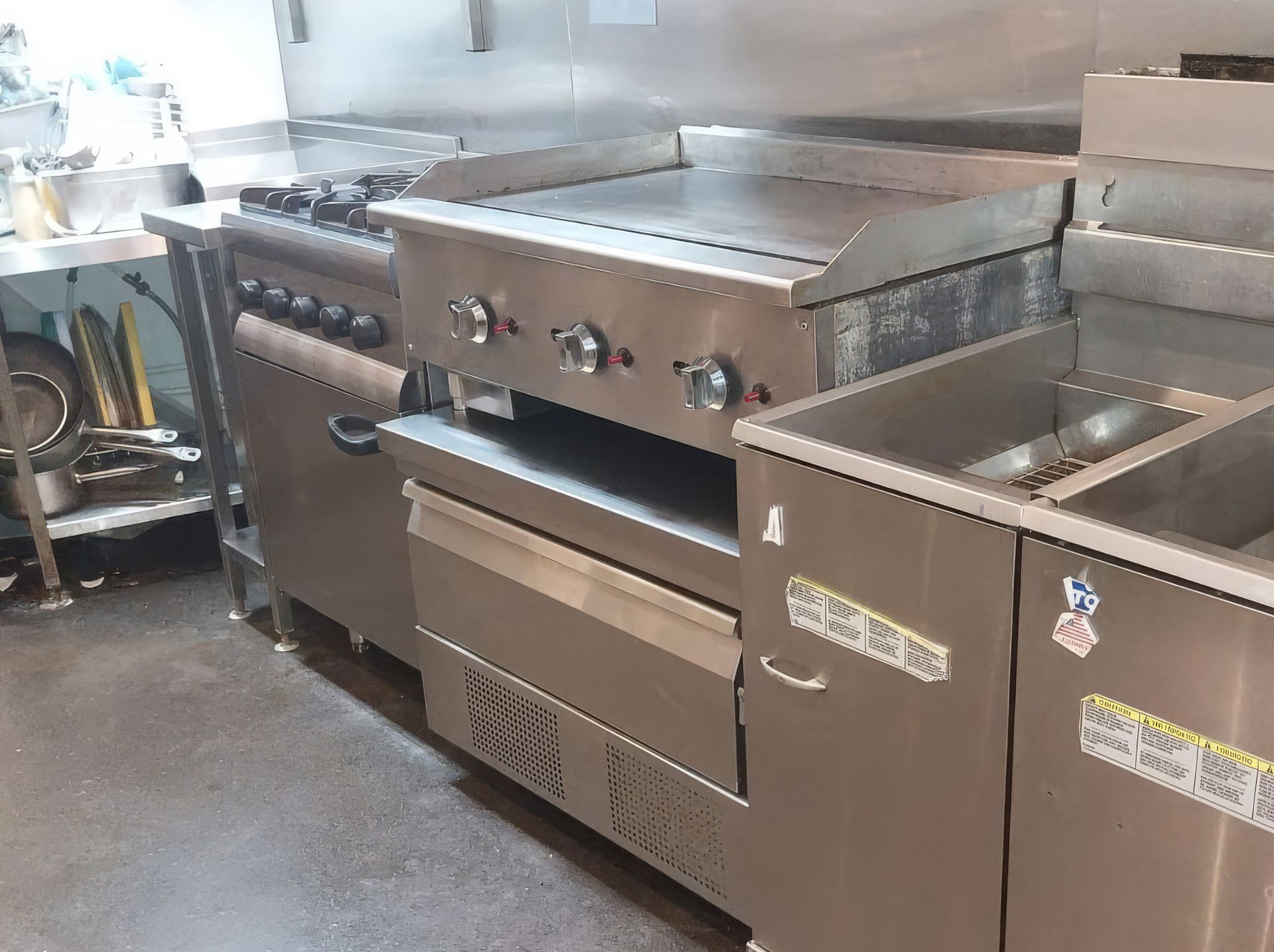 Commercial kitchen with stainless steel oven, griddle, and stove.