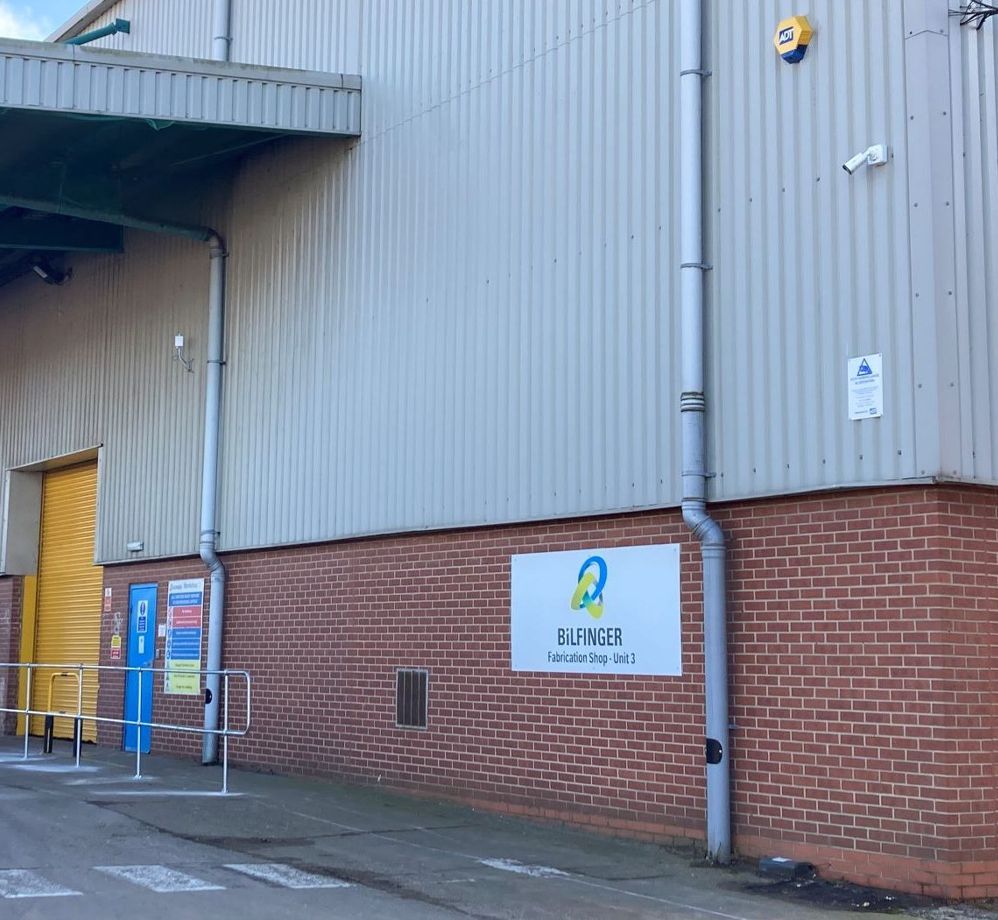 Exterior of a warehouse with a brick base and corrugated metal walls. The sign