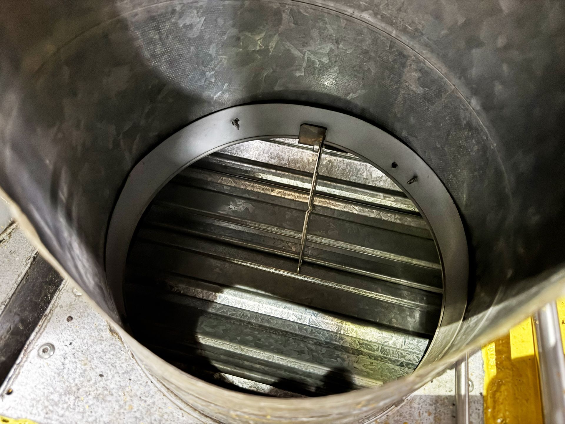 Inside view of a metal duct with a damper. The damper is made of a metal grating.