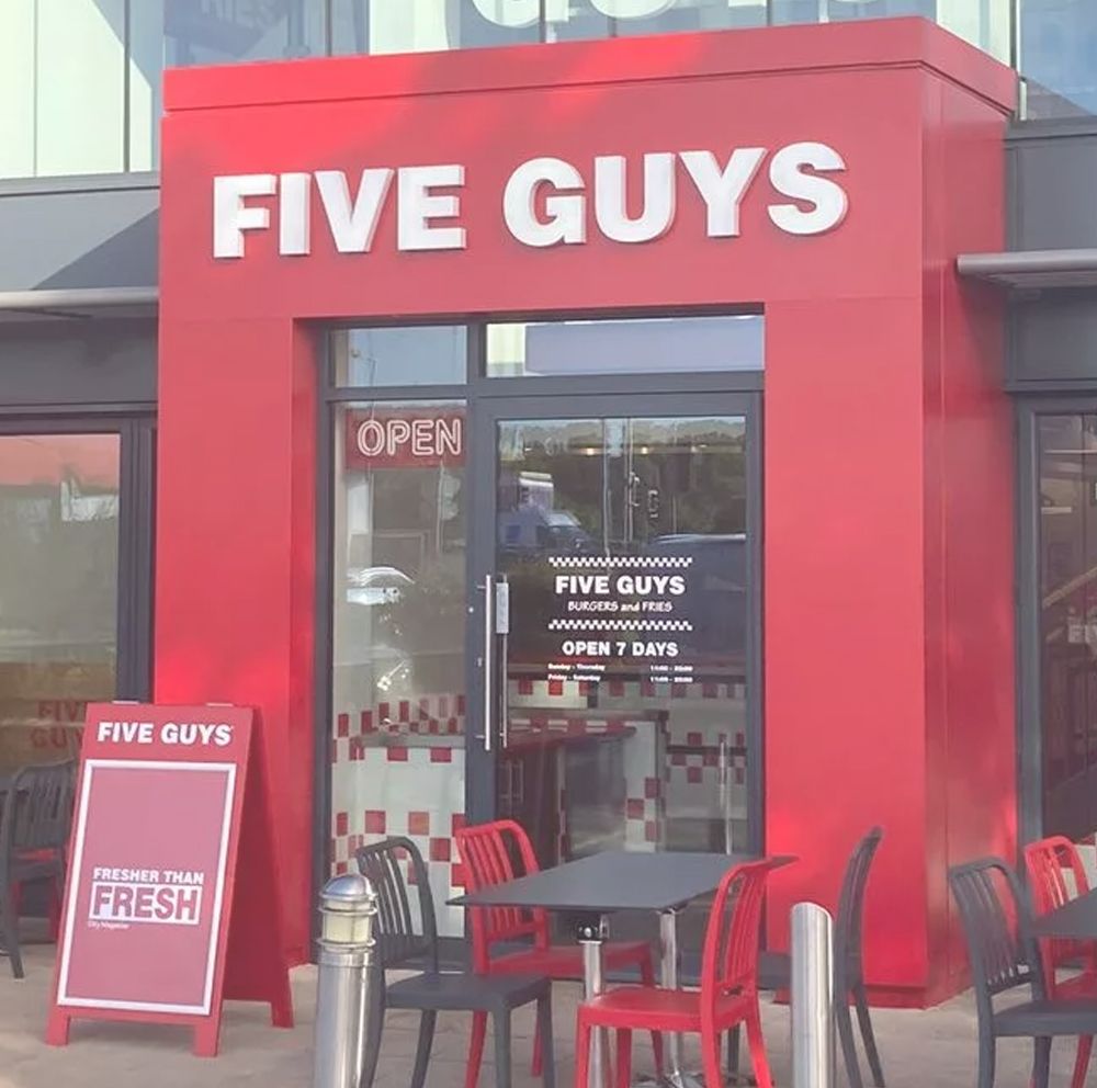 Five Guys restaurant exterior with red and white signage. Open door, outdoor seating.