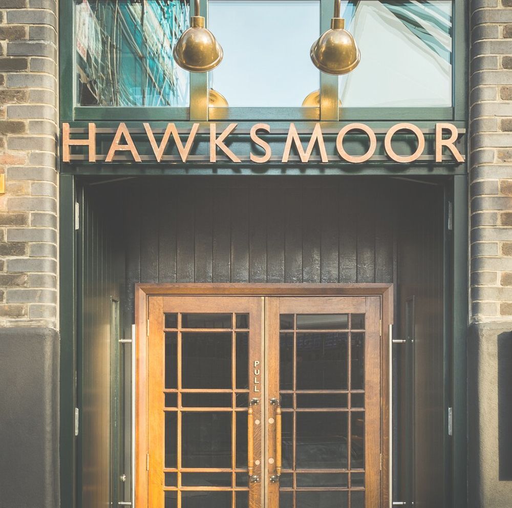 Hawksmoor restaurant entrance with wooden doors, sign, and brass lamps.