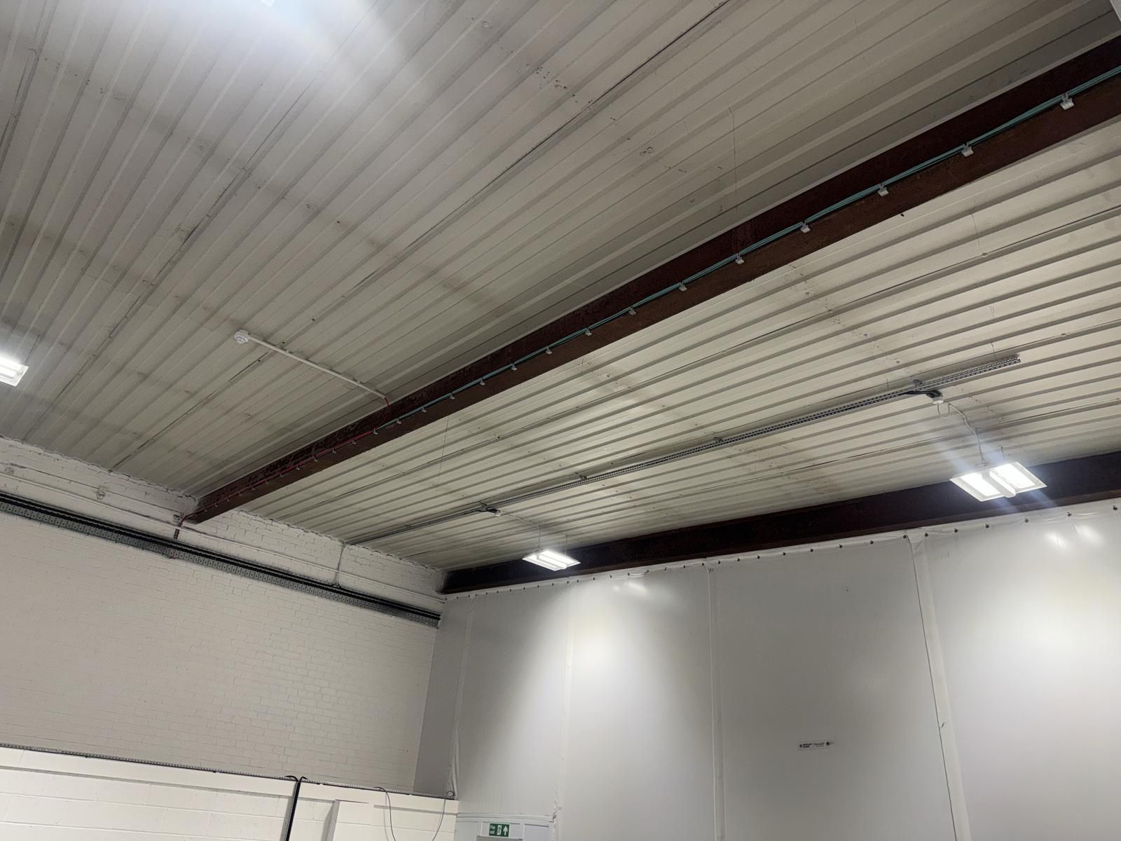 Interior view of a warehouse ceiling with metal beams and white walls.