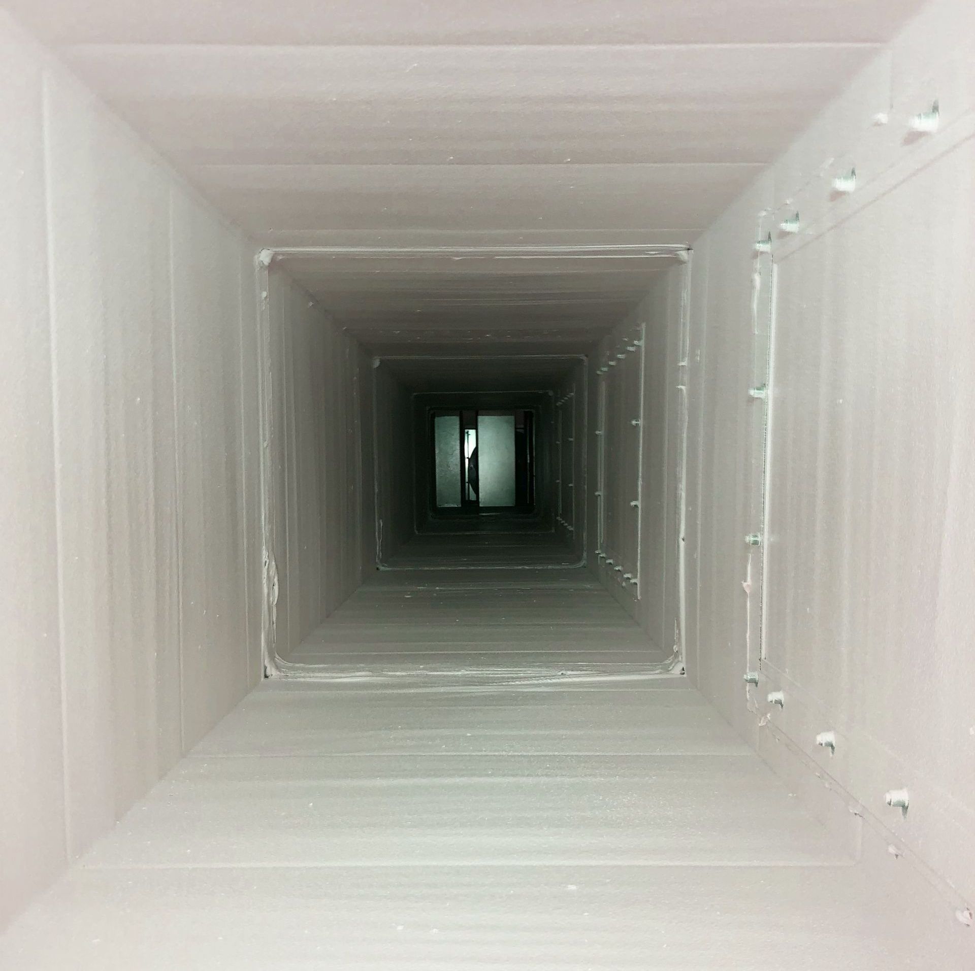 White square ventilation duct receding into darkness, with a small opening visible at the far end