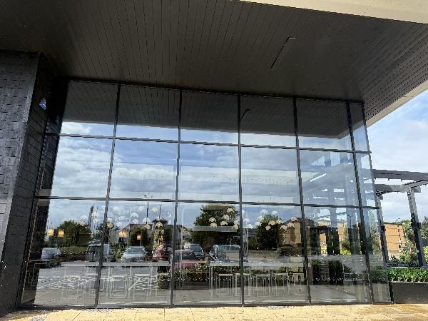 Large glass windows reflecting sky, with patio furniture and outdoor area visible inside a building.