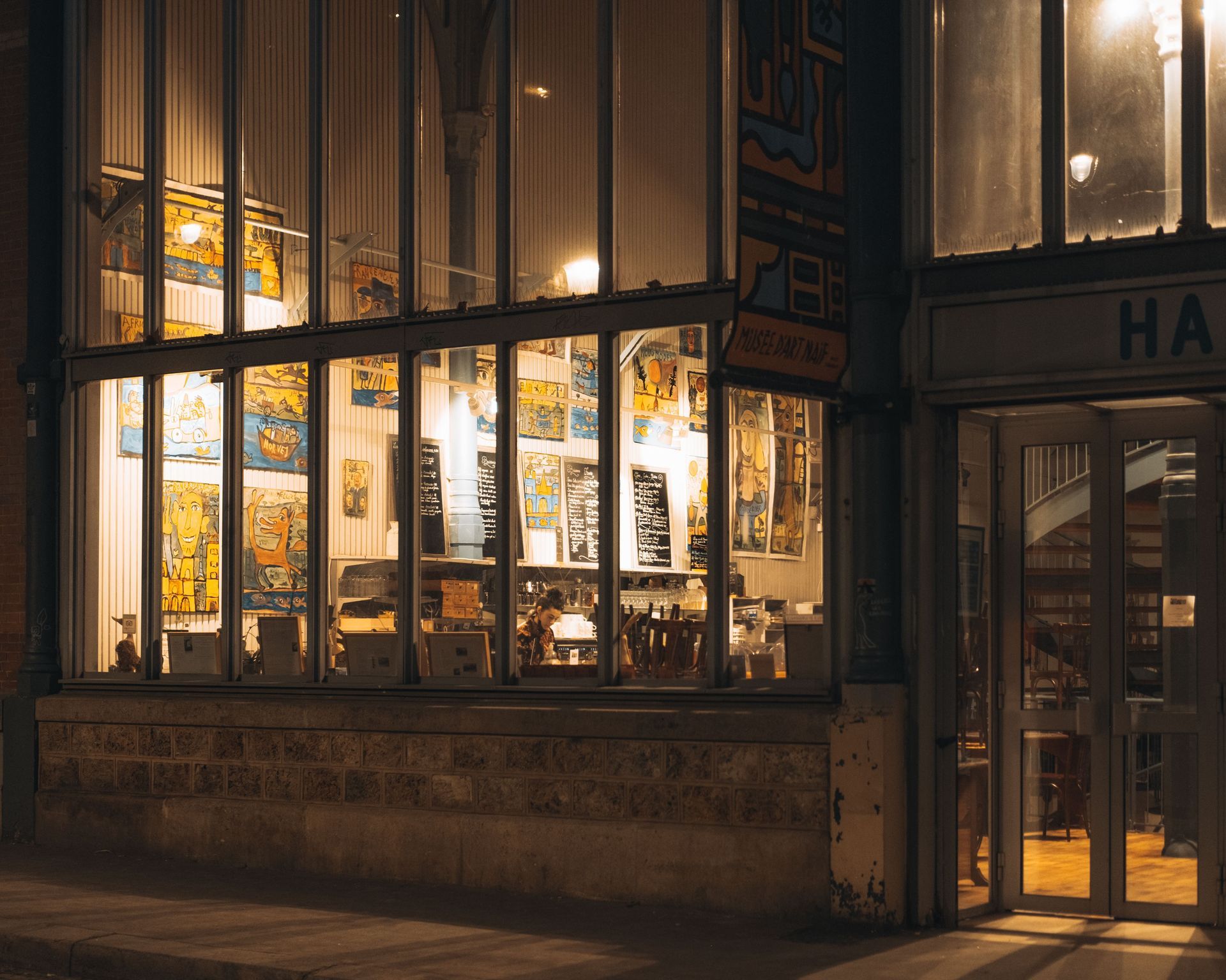 Warmly lit storefront windows at night, showing books and decor inside a cozy shop.